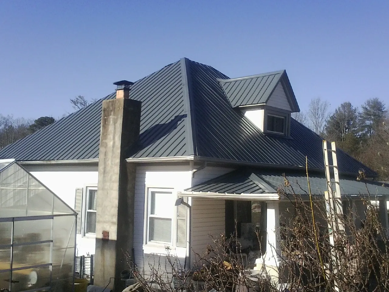 Dark blue standing seam metal roof on a white farmhouse with dormer — Slate & Tile Roof Repair by Roofing Brothers in Sanibel